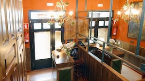 A narrow hallway with a wooden door, a small bar area with stools, and a mirror reflecting the room. - Hotel Avenida Real (Villaviciosa)