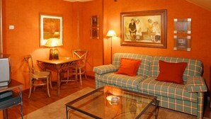 A living room with a plaid sofa, a glass coffee table, a dining table with chairs, and a painting on the wall. - Hotel Avenida Real (Villaviciosa)