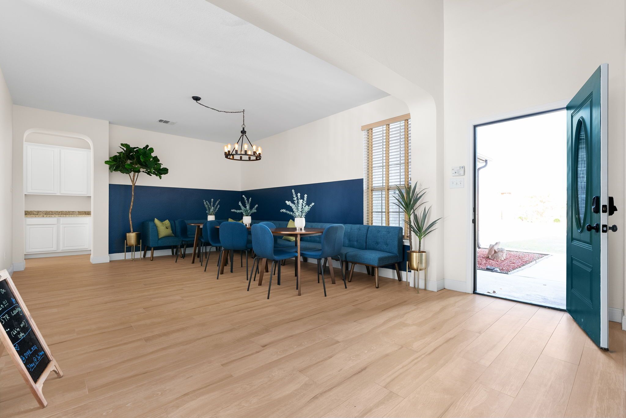 A modern interior with a blue accent wall, a chandelier, and a seating area with blue chairs and a sofa.