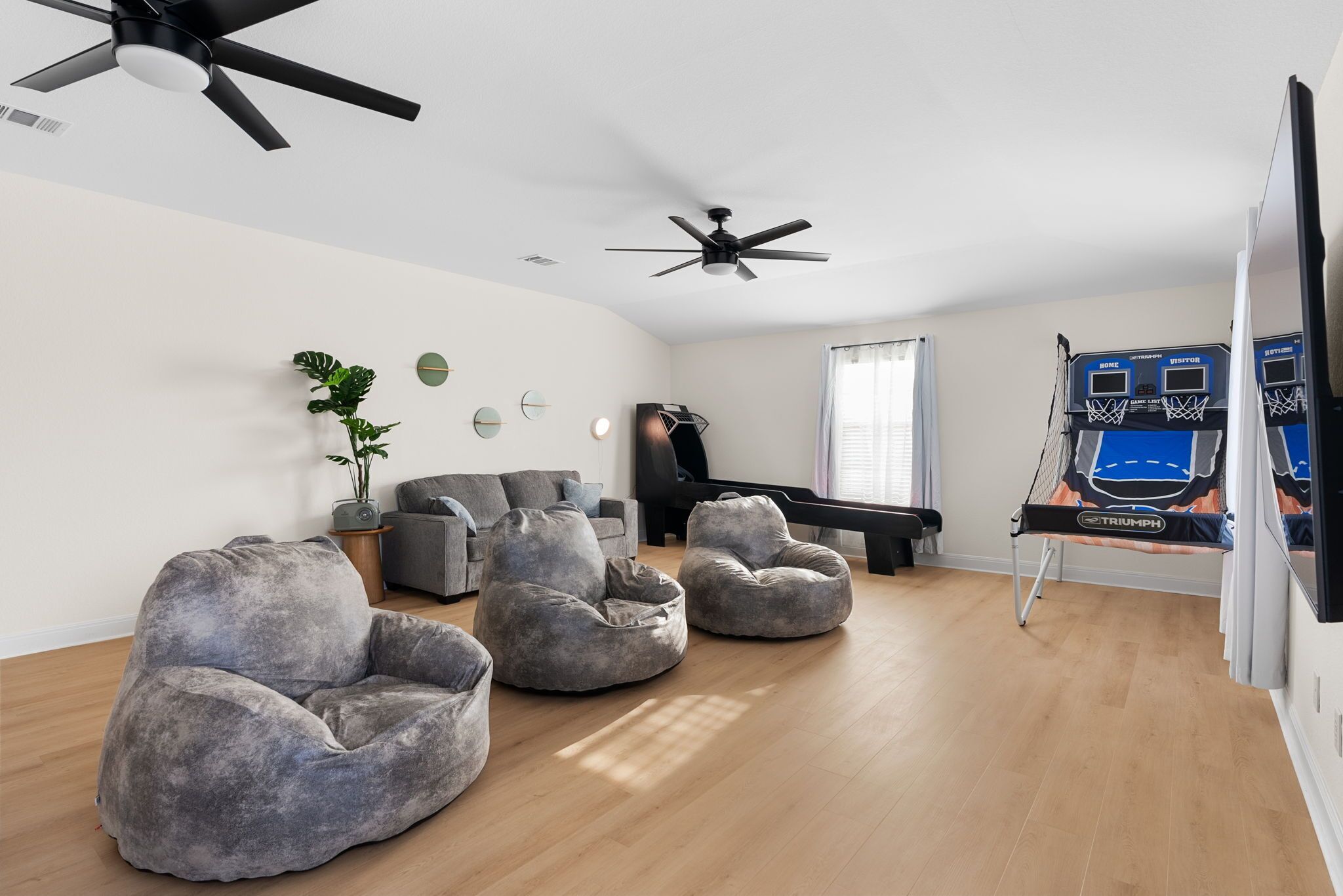 A living room with a piano, bean bag chairs, ceiling fans, and a basketball hoop.