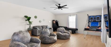 A living room with a piano, bean bag chairs, ceiling fans, and a basketball hoop.