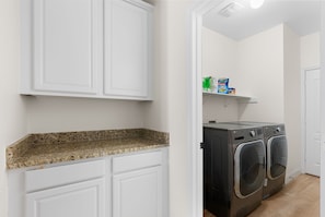 A laundry area with a washing machine, a shelf with cleaning products, and a granite countertop. - Large Groups' Luxury House Pool Sleep 22 (Round Rock)