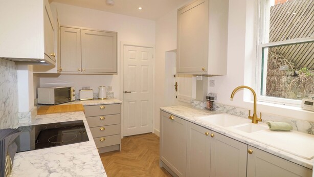A kitchen with white cabinets, a microwave, a toaster, and a sink with a gold faucet. - Crown Cottage (Belper)