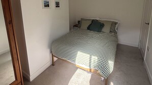 A bedroom with a checkered bedspread, a wooden dresser, and two framed pictures on the wall. - Crown Cottage (Belper)