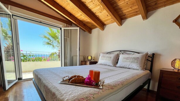 A bedroom with a bed, a nightstand, a lamp, and a view of the outdoors. - Giovanni Apartments (Igoumenitsa)