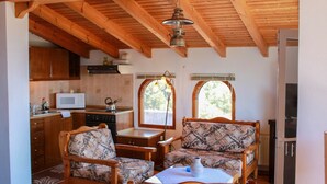 A cozy kitchen with wooden beams, a dining area with patterned furniture, and a view through windows. - Giovanni Apartments (Igoumenitsa)