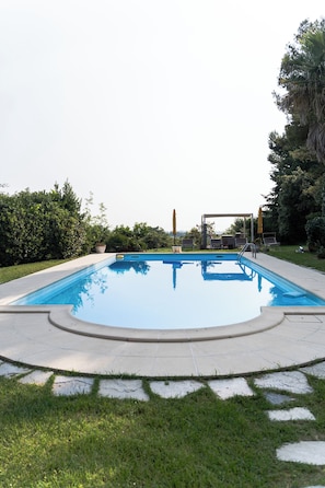 Una piscina rectangular amb un solàrium enrajolat, envoltada d'herba i arbustos.