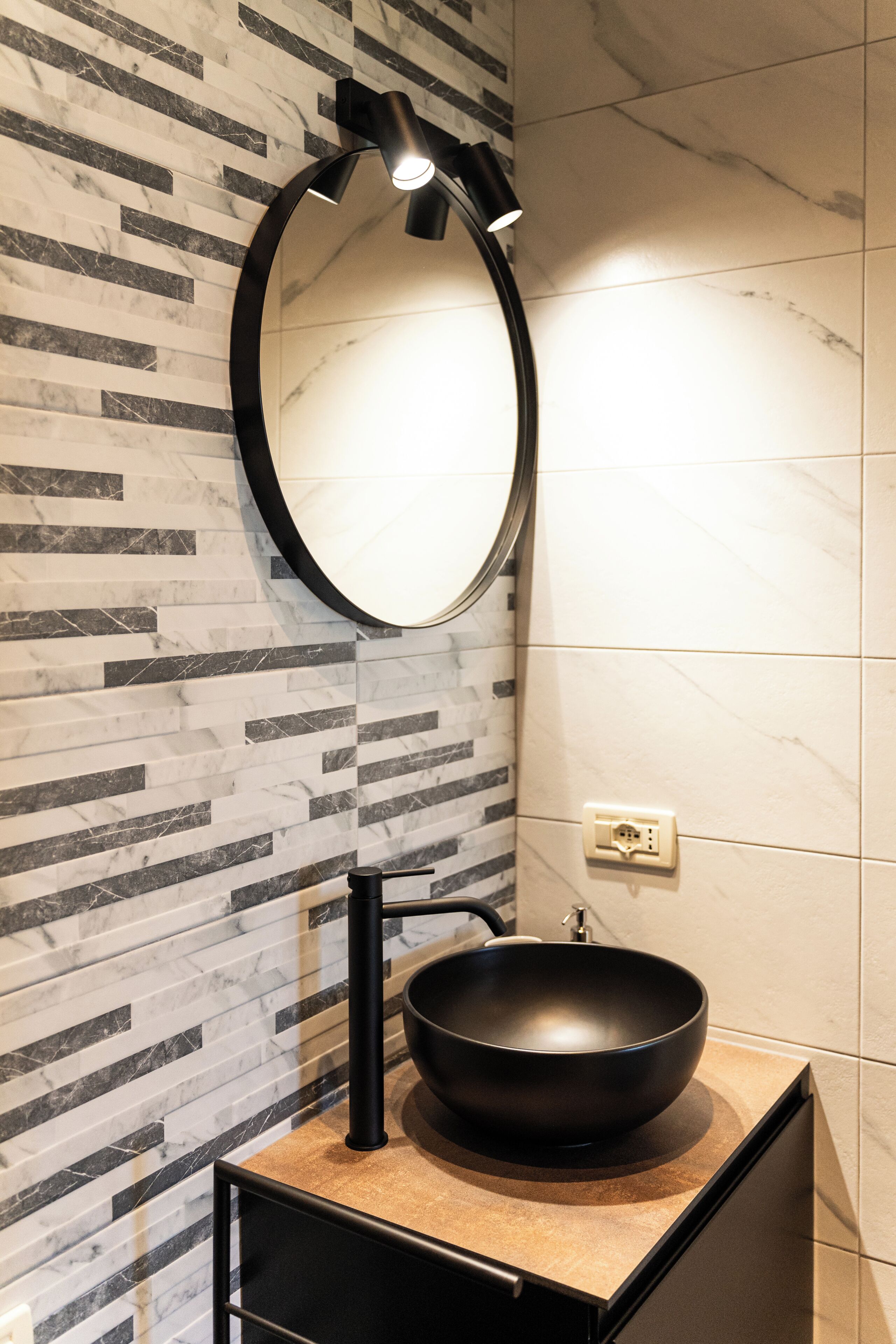 A modern bathroom with a black sink, a round mirror, and a wall with a marble pattern.