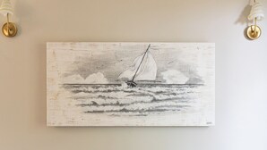 Una sala de estar con un sofá gris, un cuadro colgado en la pared de un velero y dos apliques de pared.