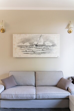 Un soggiorno con un divano grigio, un quadro appeso raffigurante una barca a vela e due applique.