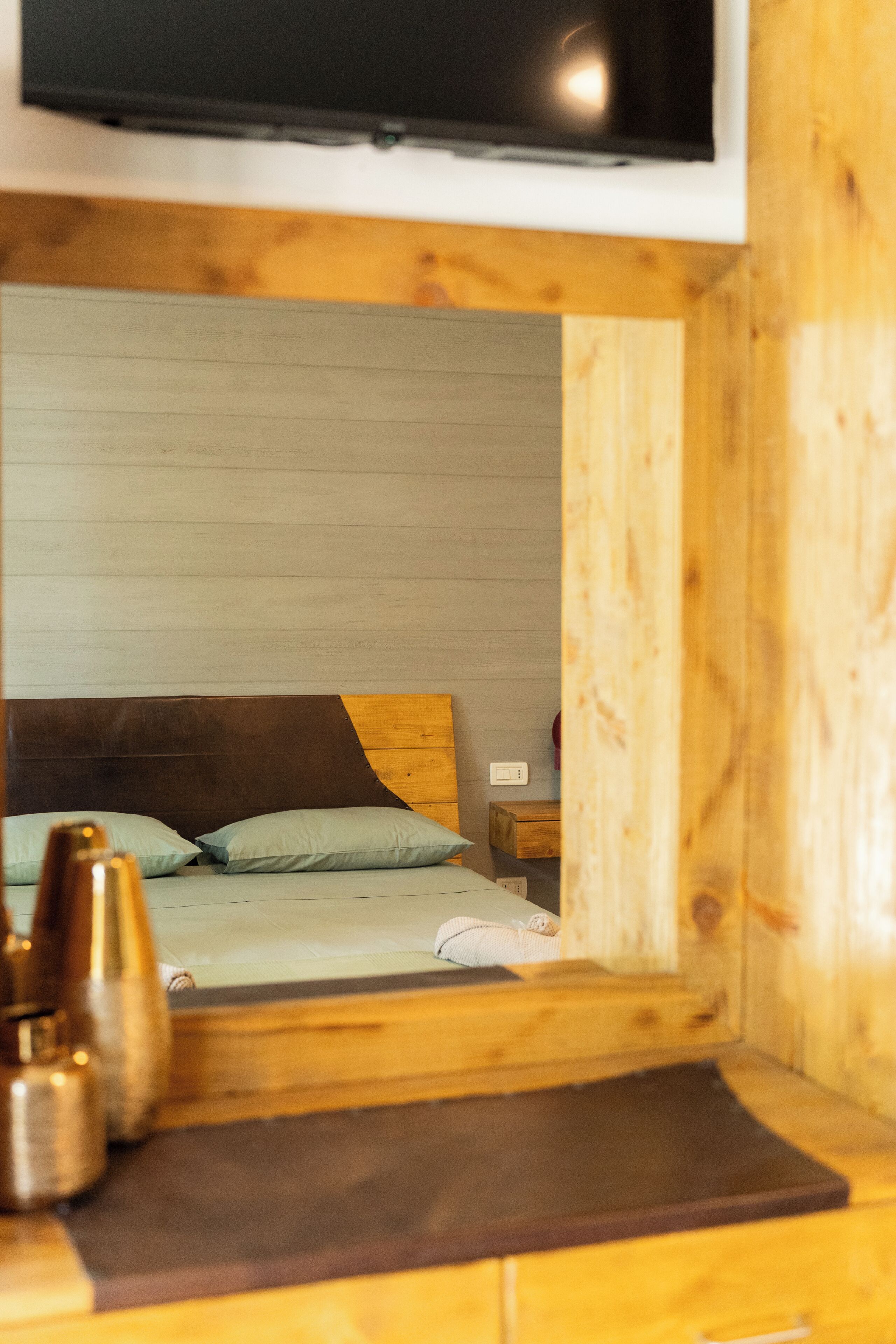 A wooden cabin-style room with a bed, a nightstand, and a television mounted on the wall.
