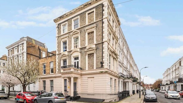A multi-story building with a classic architectural style, featuring a prominent corner entrance and a balcony. - West Kensington 1-Bed | Private Garden | Sleeps 4 (Greater London)