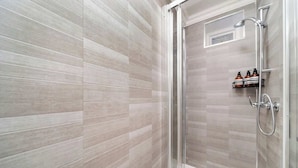 A shower with a glass door, a handheld showerhead, and a shelf with toiletries. - West Kensington 1-Bed | Private Garden | Sleeps 4 (Greater London)