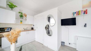 A modern kitchen with white cabinets, a microwave, a sink, and a glass table. - West Kensington Studio | 3-Min Walk to Tube | Sleeps 2 (Greater London)