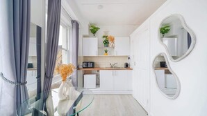 A modern kitchen with white cabinets, a glass table, and a unique wall mirror. - West Kensington Studio | 3-Min Walk to Tube | Sleeps 2 (Greater London)