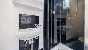 A modern bathroom with a white sink, a glass shower enclosure, and a visible toilet. - West Kensington Studio | 3-Min Walk to Tube | Sleeps 2 (Greater London)