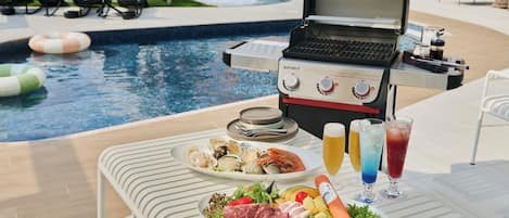 A poolside dining area with a grill, seafood platter, and drinks.