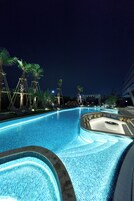 A swimming pool with a tiled edge, surrounded by palm trees and lounge chairs.
