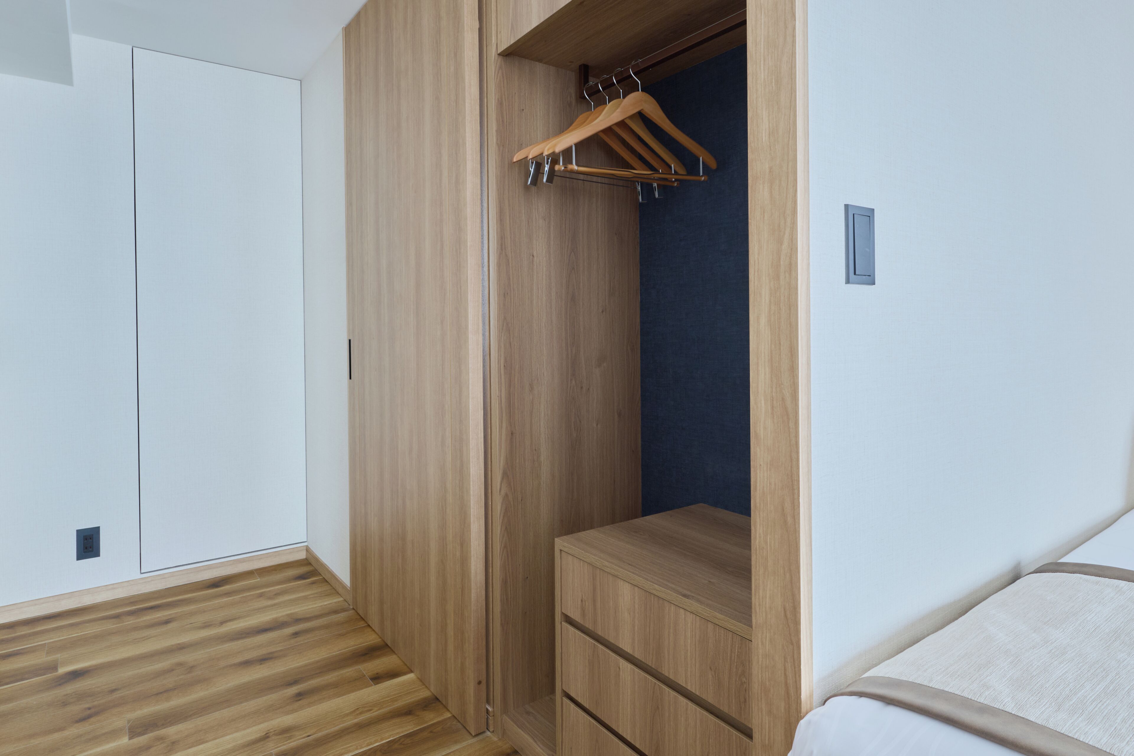 A bedroom with a wooden wardrobe, a bedside table, and a hanging wardrobe.