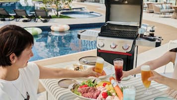 Zona de comedor junto a la piscina con una parrilla, piscina y sillas de descanso.