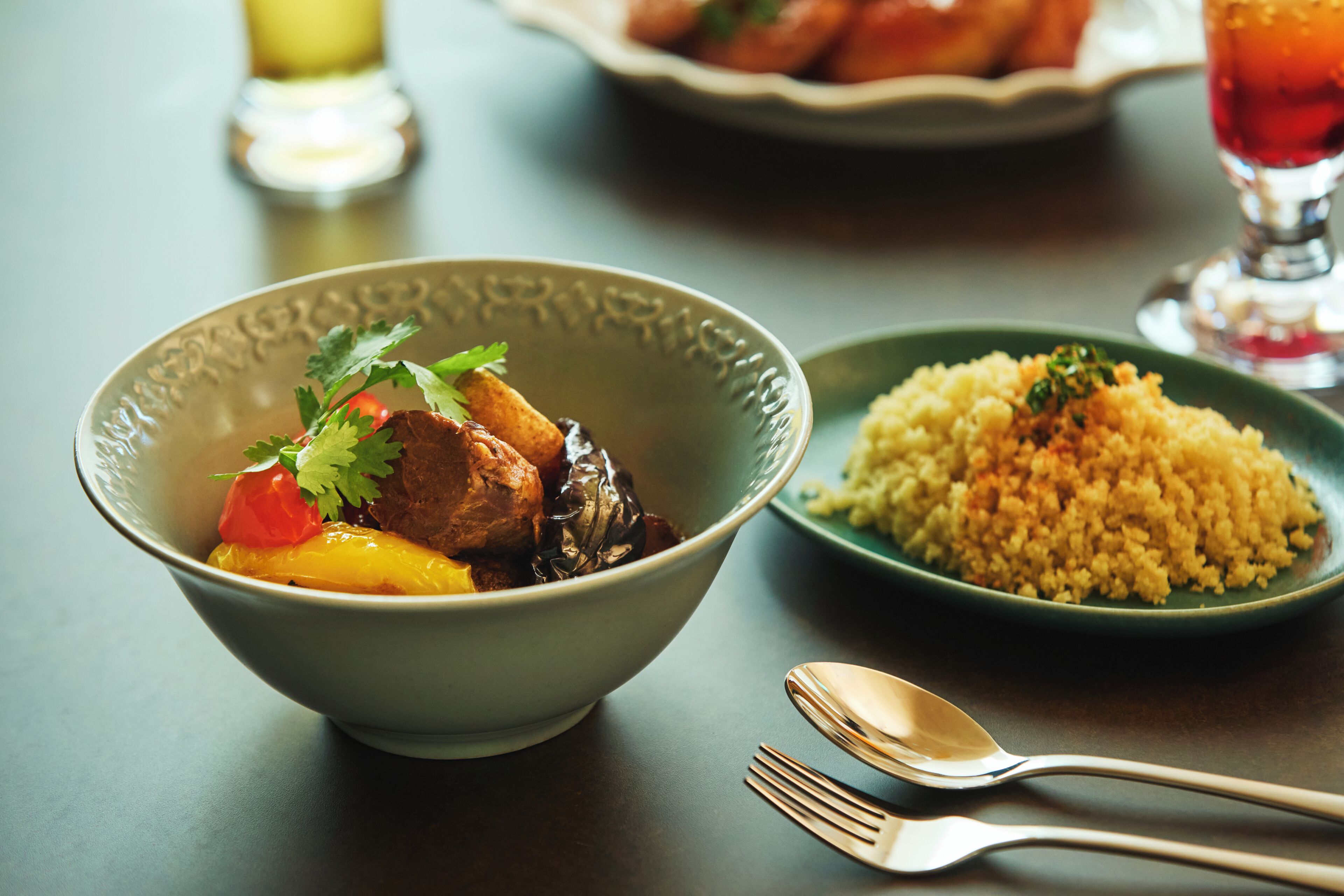 A bowl of stew with vegetables and a side of couscous on a table.