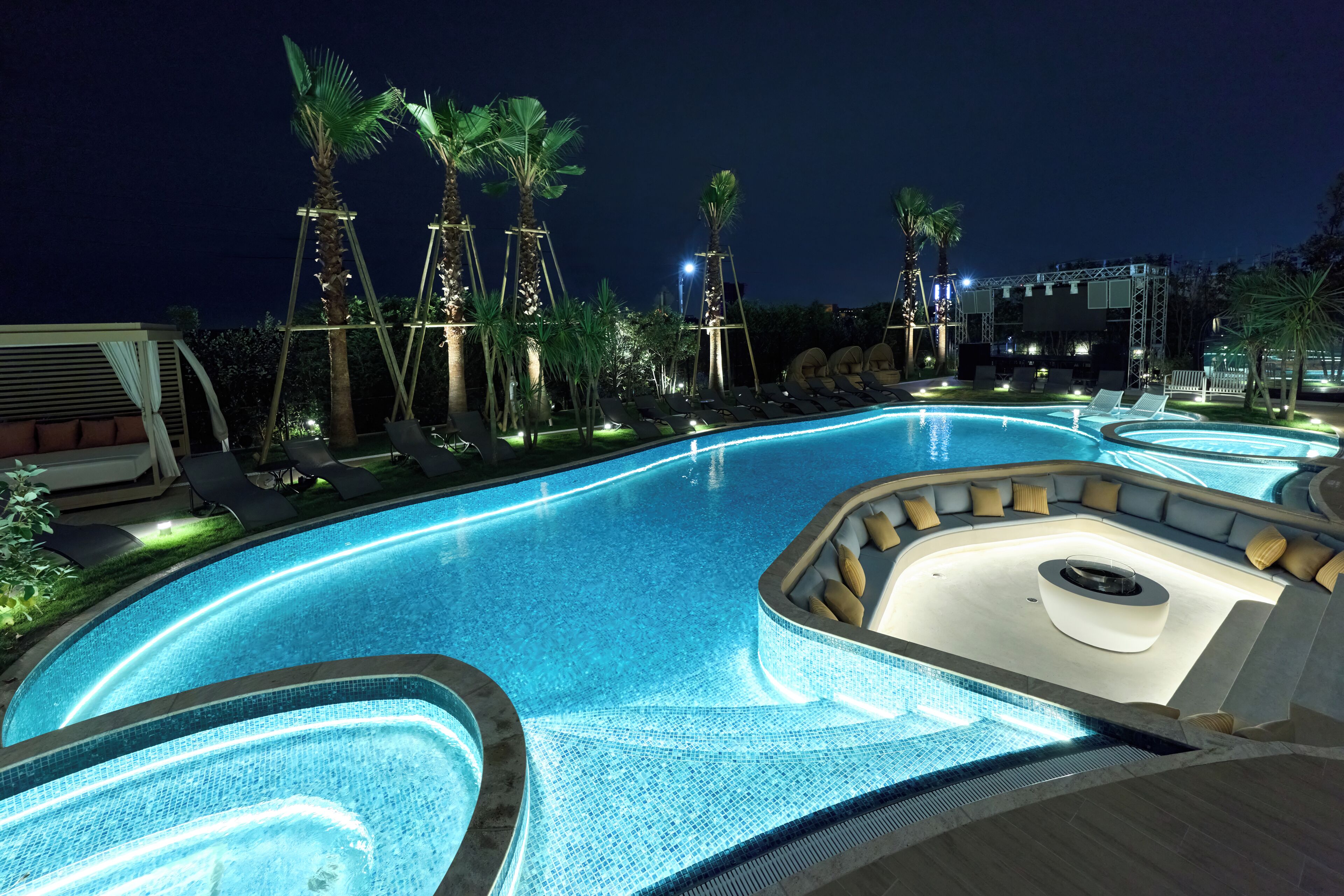 A nighttime swimming pool area with lounge chairs and palm trees.