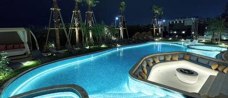 A nighttime swimming pool area with lounge chairs and palm trees.