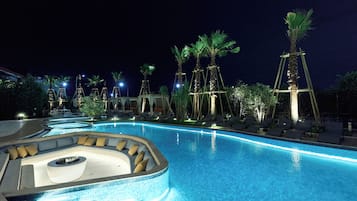 A nighttime swimming pool area with lounge chairs and palm trees.