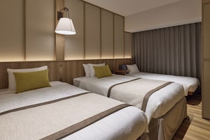 A hotel room with two beds, a bedside table, a lamp, and a curtain.