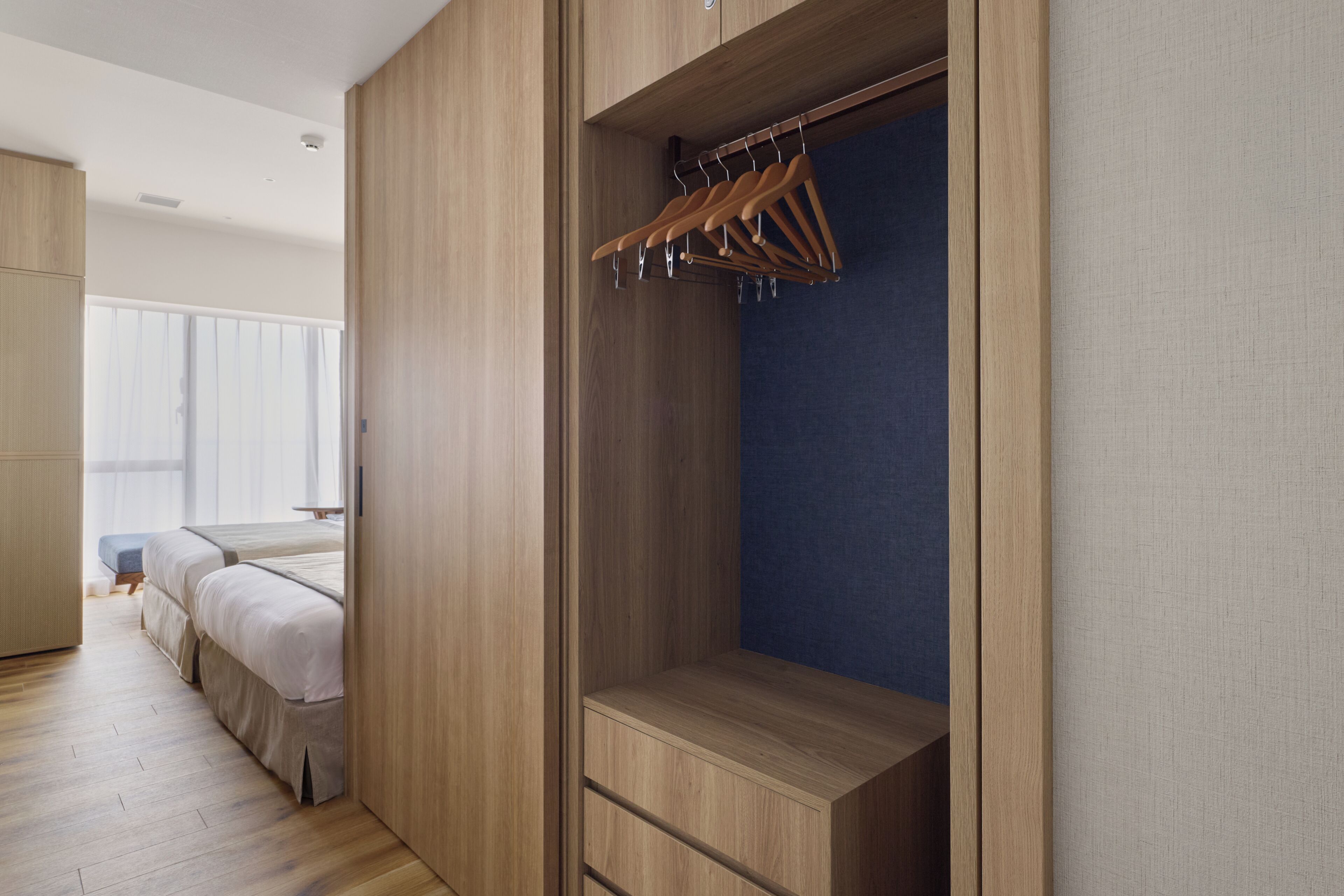 A modern bedroom with a walk-in closet, wooden flooring, and a bed with a blue headboard.