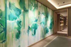 A hallway with a large abstract mural on the wall, wooden flooring, and a door leading to a room with shelves.
