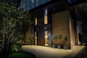 Un edificio moderno con una entrada amplia, plantas en macetas y un camino bien iluminado.