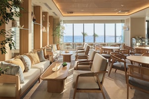 A spacious lounge area with a view of the sea, featuring a sofa set, dining tables, and wicker chairs.