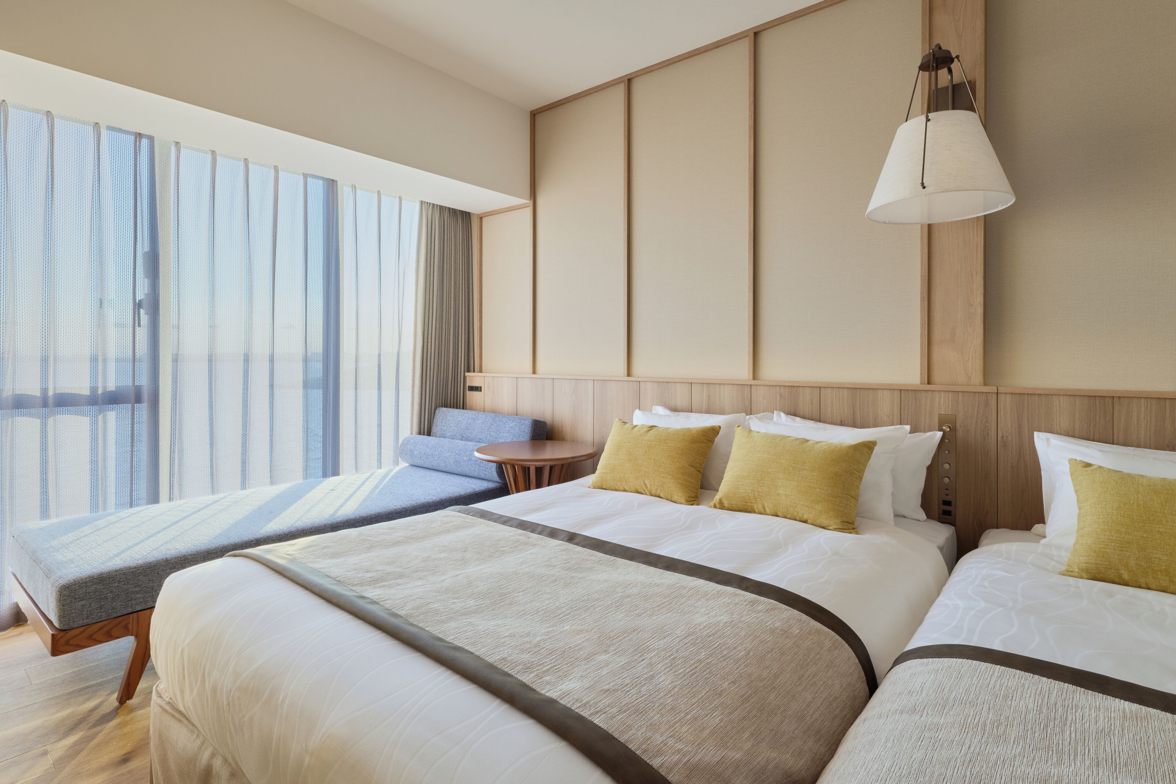 A hotel room with a large bed, a smaller sofa, a desk, and a window with curtains.
