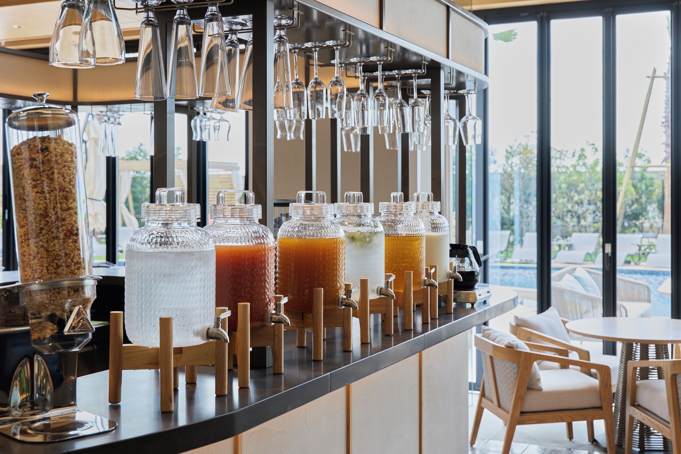 A bar area with multiple drink dispensers, a selection of glasses, and a view of the outdoors.