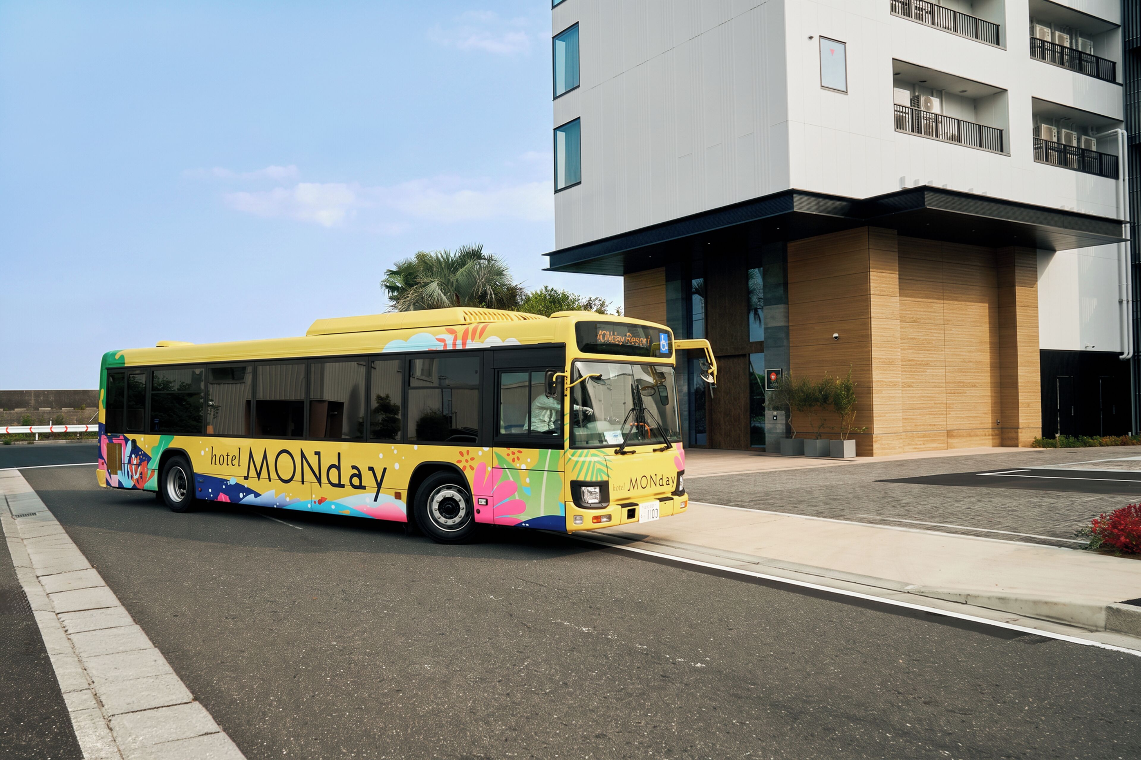 A yellow bus with 'hotel MONDAY' branding parked in front of a modern building.