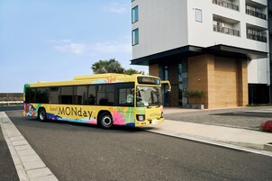 Um ônibus amarelo com a marca 'hotel MONDAY' estacionado em frente a um edifício moderno.