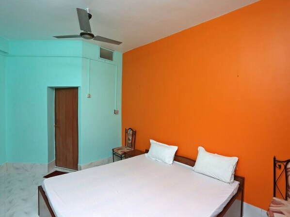 A room with a bed, a chair, a ceiling fan, and a door.
