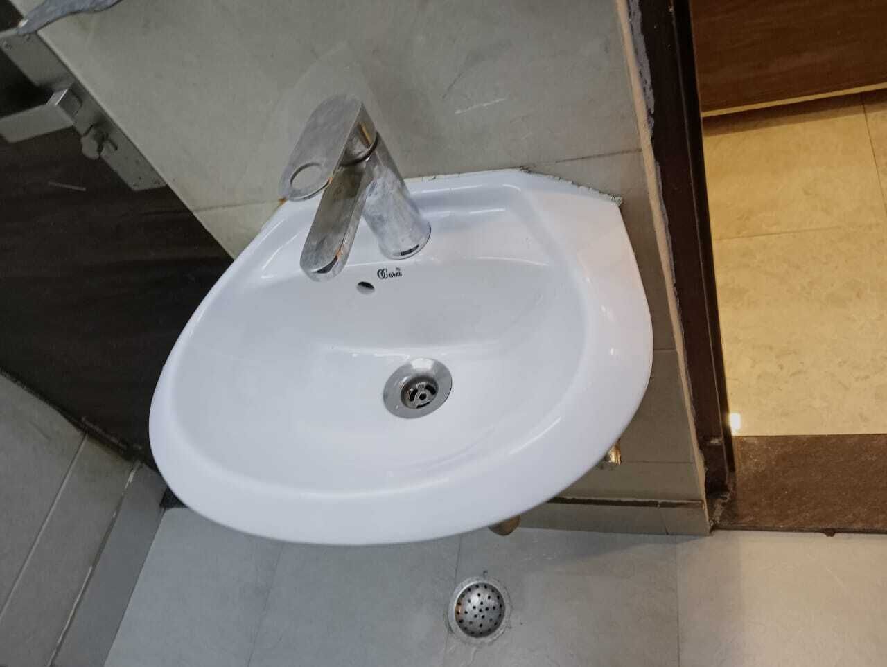 A white bathroom sink with a single faucet, a drain, and a tiled floor.