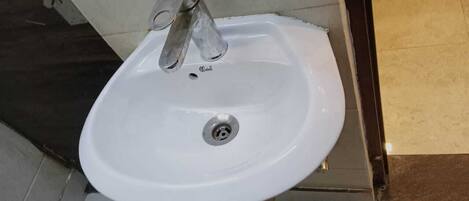 A white bathroom sink with a single faucet, a drain, and a tiled floor.