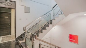 A modern interior with a glass staircase, a door with a geometric design, and a red sign on the wall. - Raj Residency Govindpuri (New Delhi)