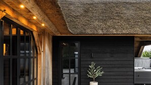 A modern building with a thatched roof, large windows, and a potted plant in the entrance. - Detached wellness cottage with private heated pool (Kortehemmen)