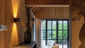 A room with a wooden ceiling, a large window, a sofa, and a table with a vase. - Detached wellness cottage with private heated pool (Kortehemmen)