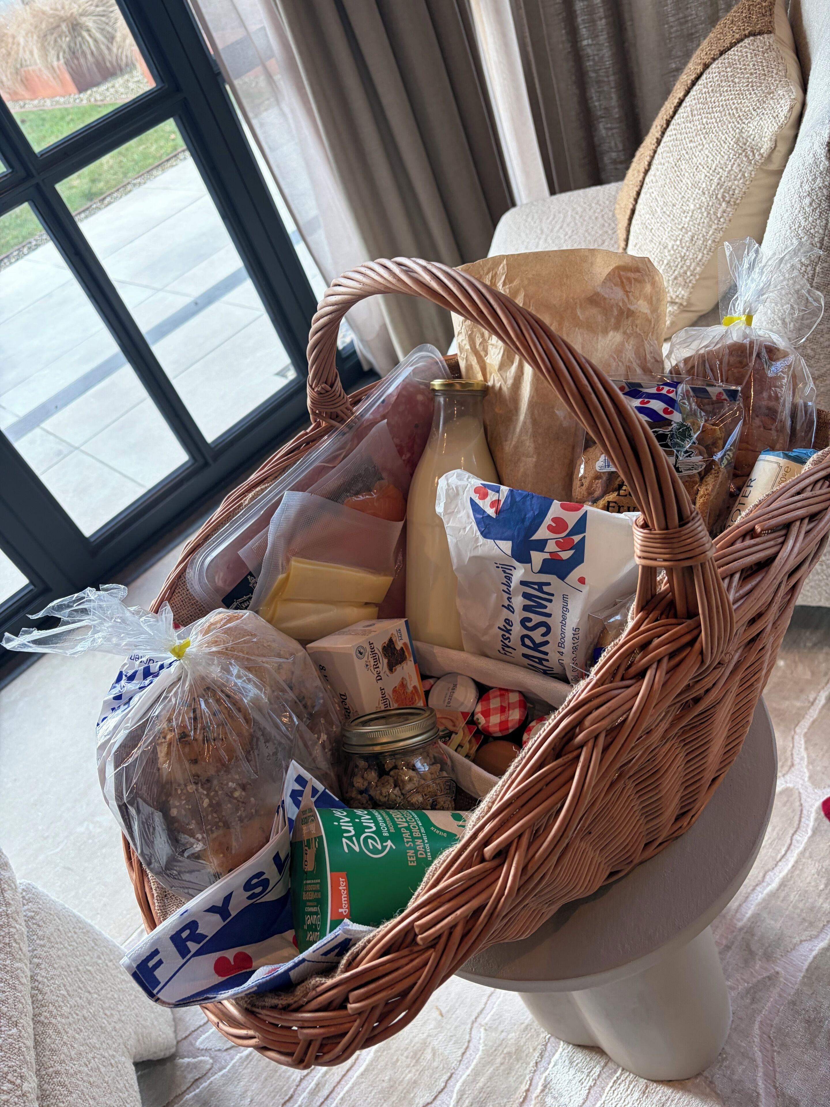 Een rieten mand gevuld met boodschappen op een witte stoel.
