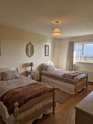 A bedroom with two beds, a mirror, a lamp, a window with curtains, and a view of the landscape. - Teach Na hAirde with Stunning Views (Carna)