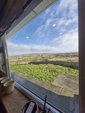 A view from inside a train or bus, looking out through a large window at a grassy landscape with stone walls and distant hills. - Teach na hAirde (Carna)