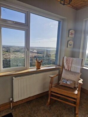 A room with a large window, a radiator, a wooden chair, and a decorative pillow. - Teach na hAirde (Carna)