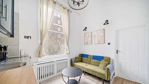 A modern kitchen with a window, a round table, a sofa, and a radiator. - West Kensington 1-Bed | 3-Min Walk to Tube | Sleeps 4 (Greater London)