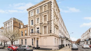 A multi-story building with a classic architectural style, featuring a prominent entrance with columns and a balcony. - West Kensington 1-Bed | 3-Min Walk to Tube | Sleeps 4 (Greater London)