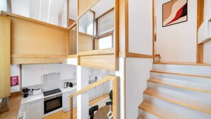 A modern kitchen with wooden cabinets, a dining area, and a staircase. - Fulham Split-Level 1-Bed Studio | Sleeps 4 (Greater London)